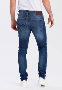Slim-fit blue denim jeans with a light wash, two back pockets, and a brown leather patch on the waistband. Clean design, no visible patterns.