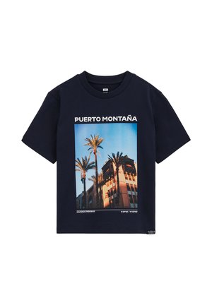 Marineblå T-shirt med grafik af palmer og en soloplyst bygning, teksten "Puerto Montaña" og geografiske koordinater under billedet.