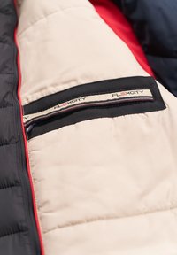 Gefütterte Jackeninnenseite in Beige, Schwarz und Rot; bietet eine schwarze Tasche mit "FLEXCITY"-Label und kontrastierender Textur.