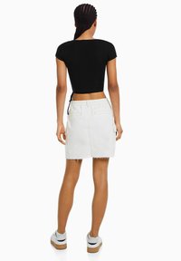 Černý kratký top, bílá denimová sukně se třepeným lemem a dvěma zadními kapsami, v kombinaci s bílými teniskami s černým akcentem.