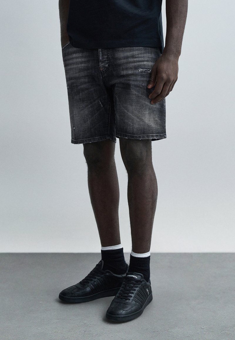 Črne jeans kratke hlače z obrabljenimi detajli, sproščenim krojem in petimi žepi. Kombinirane s črnimi supergami in nogavicami z belimi poudarki.