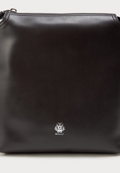 Schwarze Ledertasche mit glatter Textur, mit einem silbernen Logo am Boden. Das Design ist quadratisch mit einem Reißverschluss.