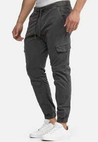 Gray cargo joggers in brushed cotton fabric, featuring elastic ankle cuffs, side pockets, and a drawstring waist. Paired with white sneakers.