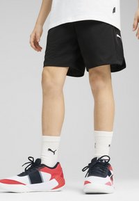 Czarne siatkowe szorty o teksturowanym wykończeniu. Białe logo Puma z boku. W połączeniu z czerwono-biało-czarnymi butami sportowymi i białymi skarpetkami.