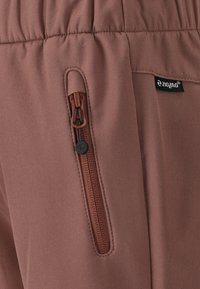Brune atletiske bukser med en side lynlås lomme, elastisk talje og en glat, let stoftekstur. Logotag synligt på stoffet.