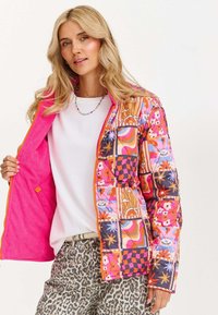 Pikowana kurtka z żywym patchworkiem w kolorze różowym, pomarańczowym i niebieskim, zdobiona wzorami kwiatowymi i geometrycznymi. Wykończona jasnoróżowym sztruksem.
