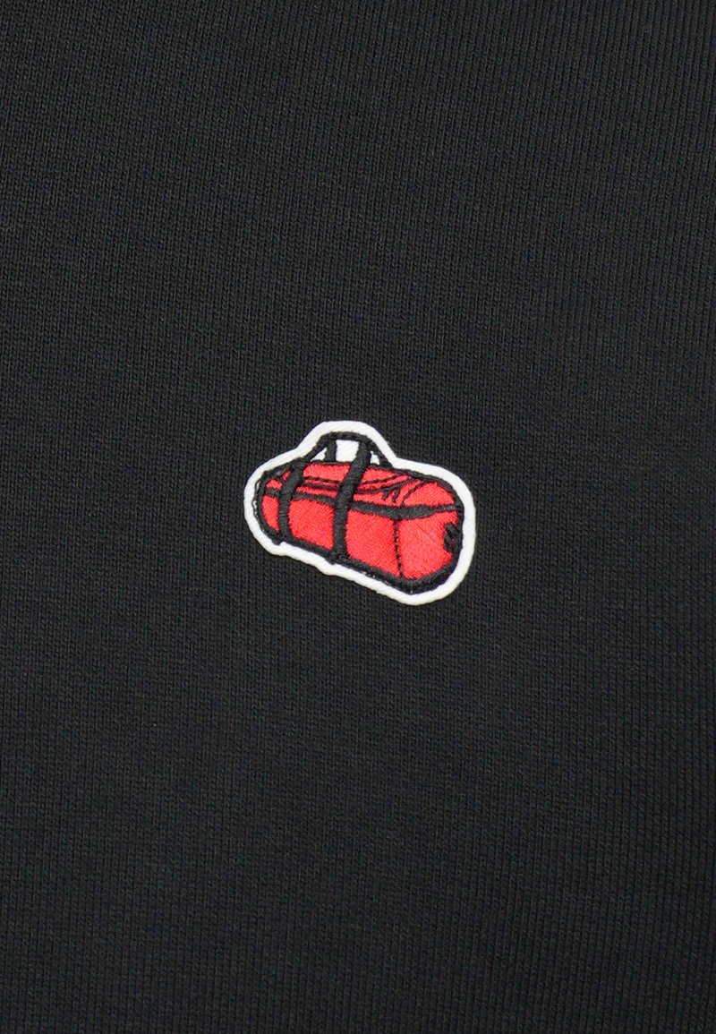 Petite valise de sport rouge avec broderie et poignées noires sur fond en tissu noir.