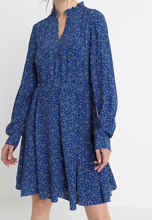 Robe bleue à manches longues avec petit motif floral blanc, col volanté, taille cintrée et jupe évasée.