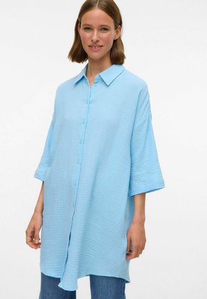 Light blue, oversized shirt made of textured fabric. Features a collar, button front, and three-quarter length sleeves. Casual design.
