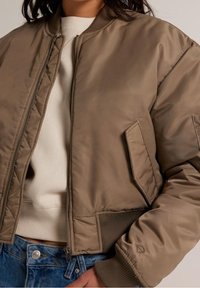 Khaki bomber jacket s zipem, žebrovanými manžetami a náprsní kapsou. Hladká, matná látka s přiléhavým střihem.