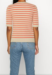 Beiger gestreifter Kurzarmpullover mit abwechselnden orangefarbenen Linien, gerippte Struktur, tailliertes Design, kombiniert mit hellblauen Jeans.