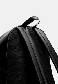 Zaino nero con un esterno in pelle testurizzata, schienale in mesh imbottito e spallacci regolabili in tessuto web. Include una maniglia superiore per il trasporto.