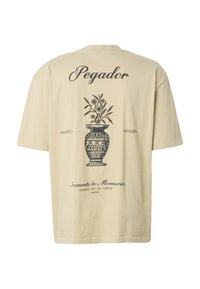 Beige t-shirt med en sort dekorativ vaseillustration og blomstergrene, med ordene "Pegador," "Moments to Memories," og "Memories that last forever."