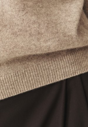 Beige cashmere sweater with a fine knit texture and ribbed hem, partially overlapped by a brown fabric below.