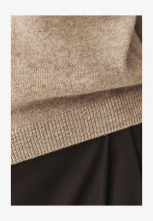 Beežist cashmere särk peene kudumise tekstuuriga ja sooniku äärisega, osaliselt katab pruun kangas all.