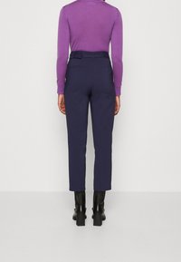 Marina skräddarsydda byxor med smal passform, som har en slät yta och bakfickor, kombineras med en ljuslila långärmad topp och svarta klackstövlar.