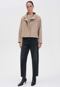 Beige cropped jack met een zachte stof en hoge kraag, gecombineerd met zwarte rechttoe rechtaan jeans en hoekige zwarte enkellaarsjes.