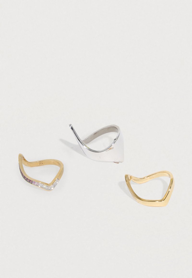 Három gyűrűs szett: egy ezüst és két arany. Az arany gyűrűk hullámos mintázatúak; az egyikbe átlátszó és rózsaszín kövek vannak beágyazva. Simára csiszolt felület.