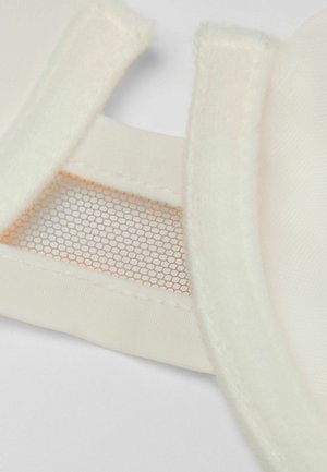 Měkká béžová látka s detaily z mřížky a plyšovým lemováním okrajů, s texturovaným povrchem a viditelným prošíváním pro strukturu a podporu.