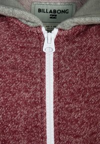 Burgundská mikina na zip s šedou fleecovou kapucí, s bílým zipem a texturovaným designem látky. Logo Billabong na štítku.