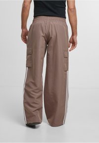 Bruna cargobyxor med avslappnad passform, som har sidofickor och vita ränder längs sidorna. Elastisk midja för komfort.