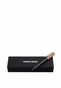 Stylo à bille noir avec une prise texturée et des accents marron, placé à côté d'une boîte noire avec le logo "HUGO BOSS" en blanc.