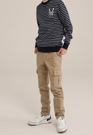 Marine gestreepte sweatshirt met witte strepen, beige cargobroek met zijzakken en witte sneakers met marine accenten. Casual outfit ontwerp.