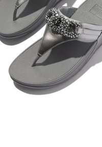 Grijze teenslippers met een gestructureerde zool en een metalen bandje versierd met zwarte strassteentjes, met een klassiek T-banddesign.