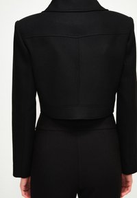 Zkrácený černý blazer s límcem, dlouhými rukávy, vypasovaným střihem a jemnými detaily prošívání na zadní straně, vyrobený z textured látky.