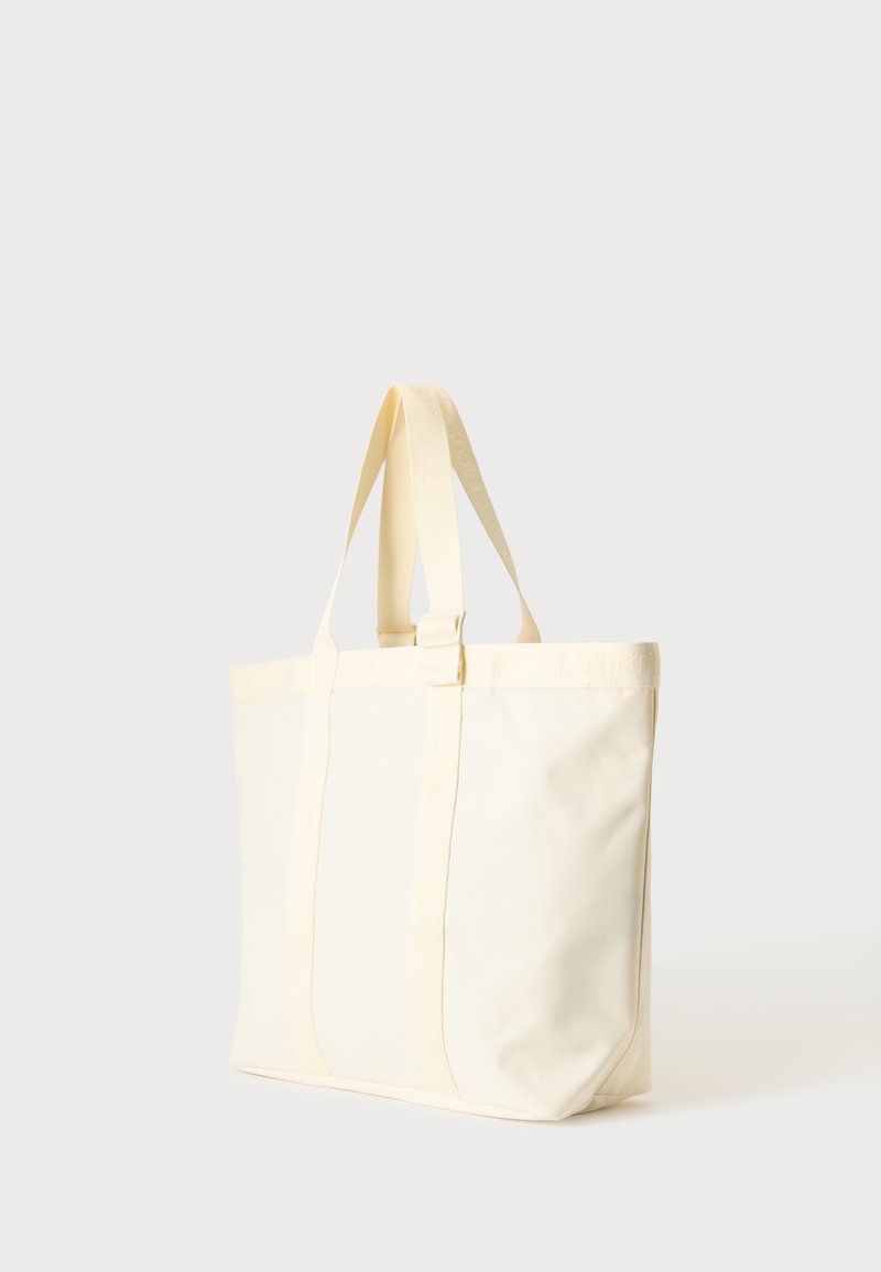 Grande borsa tote in tela color crema con due manici, in piedi su uno sfondo chiaro e semplice.
