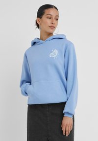 Felpa leggera blu chiaro realizzata in tessuto morbido, con tasca frontale, cappuccio con cordino e una grafica di farfalla bianca sul petto.