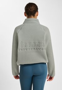 Grijze fleece pullover met hoge kraag, gestructureerde stof en geborduurd "hummel" logo op de achterkant. Het cropped ontwerp vormt een mooie aanvulling op strakke leggings.