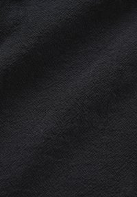 Tissu noir avec un motif subtil en losange texturé et de doux plis créant des variations d'ombre sur la surface.