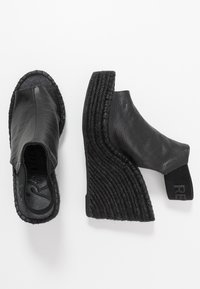 Sandalias de cuña de cuero negro con textura similar al yute tejido. Presentan puntera cerrada, talón abierto y tira elástica en el tobillo.