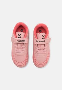 Svijetlo ružičaste tenisice s teksturiranom površinom, koje imaju čičak trak i crne akcentne detalje, uključujući "hummel" logo i zigzag uzorke.