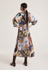Langes, gemustertes Kleid mit lockerer Passform, das große Blumenmuster in Braun, Blau und Pink auf einem hellen Hintergrund und eine geraffte Taille zeigt.