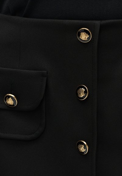 Μαύρο ύφασμα με κουμπιά με χρυσή επένδυση που φέρουν περίπλοκα ανάγλυφα έμβληματα, μαζί με ένα αντίστοιχο κουμπί σε τσέπη με καπάκι.