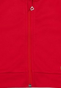 Giacca zip-up rossa con zip in metallo, orlo elasticizzato e tessuto testurizzato. Include un piccolo logo nell'angolo in basso a destra.