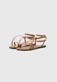 Bruine leren sandalen met dunne banden, platte zolen en vergulde hardwareaccenten. Open teen ontwerp met een minimalistische stijl.