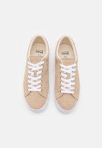 Sneakers in suede beige con lacci bianchi, punta rotonda e suola in gomma bianca. L'interno presenta una soletta con marchio. Nessun ulteriore accento presente.