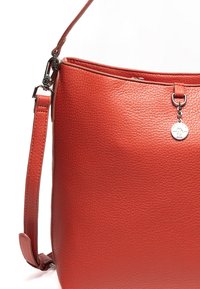 Rød tekstureret læderhåndtaske med en enkelt justerbar skulderrem, lynlåslukning og en dekorativ metalcharme hængende foran.