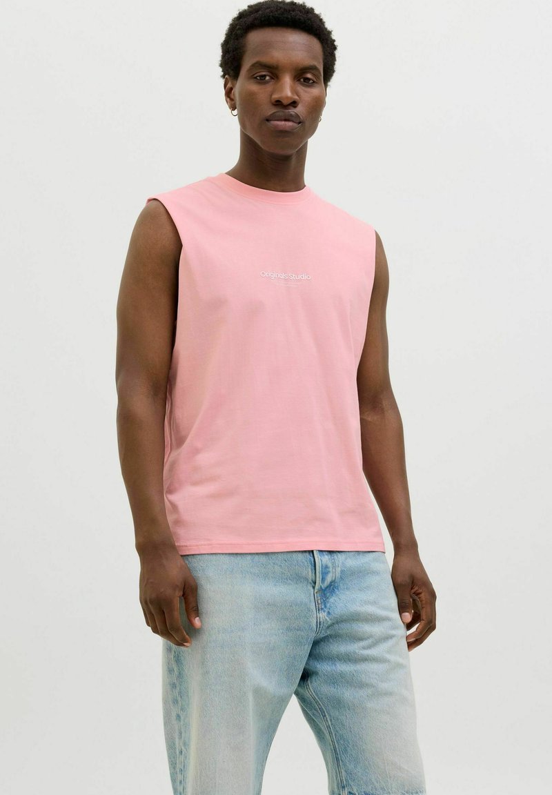 Rosa ärmlös t-shirt med rund halsringning och "Originals Studio" tryckt i vitt. Bärs tillsammans med ljusblå denimshorts.