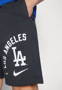 Harmaat urheilushortsit, joissa on valkoiset "LOS ANGELES" ja "LA" -grafiikat, valmistettu pehmeästä kankaasta, sivutaskut ja Nike-logo.