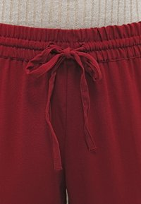 Red elastic waistband pants featuring a drawstring tie, crafted from a smooth, lightweight fabric suitable for casual wear.
