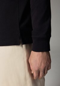 Svart långärmad skjorta med texturerad tyg, sidsplit och åtsittande manschetter, ihopparad med en ljusfärgad, släthet tyg underdel.
