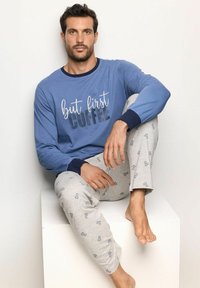 Camicia a maniche lunghe blu con il testo "ma prima il caffè", abbinata a pantaloni da pigiama grigi chiari con un motivo di caffettiere. Vestibilità casual, tessuto morbido.