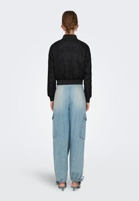 Black satin bomber jacket with ribbed cuffs and hem, paired with light blue baggy jeans featuring large side pockets and tapered cuffs.