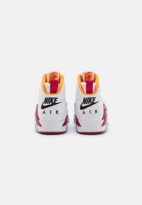 Tenisky Nike Air s bielym zvrškom, oranžovými doplnkami, červenými detailmi a čiernym brandingom. Majú polstrovaný golier a priehľadnú gumovú podrážku.