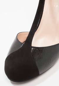 Chaussure à talon haut noire composée d'un mélange de daim et de cuir verni texturé. Bout rond avec une finition lisse et brillante d'un côté.