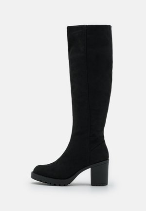 Botte noire montant jusqu'au genou avec talon bloc et semelle crantée, fabriquée en matériau type daim, présentée de profil sur fond uni.